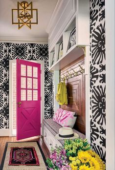 a bright pink door sits in front of a black and white wallpapered entryway