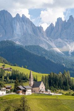 an old church sits in the middle of a green valley with mountains in the background