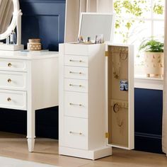 a white jewelry cabinet sitting in front of a window next to a dresser and mirror