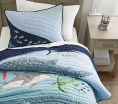 there is a bed with a blue quilt on it and two pillows that have dolphins on them