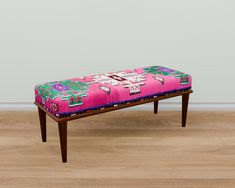 a bench with a pink and green patterned seat cover on it's legs, in front of a white wall