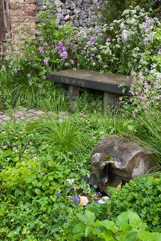 a stone bench sitting in the middle of a garden filled with lots of flowers and plants