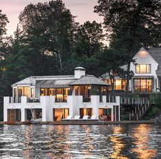 a large white house sitting on top of a lake next to a lush green forest