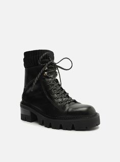 Black leather combat boot. The style features a mid-shaft, a rounded toe and a low rubber heel with a rugged, chunky lug sole with a stacked detailing. It has a snug-fitting vamp, lace closure in the color of the boot and a pull-tab on the back, making it easy to put on. The upper part of the shaft is made of knit material. Why follow this trend?These combat boots are essential items for the season! They feature a chunky lug sole in a super versatile tone and are a guarantee of comfort and style Black Leather Combat Boots, Genuine Leather Boots, Combat Boot, Rounded Toe Boots, Rubber Heels, Lug Sole, Knitting Materials, Lace Closure, Leather And Lace