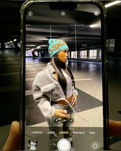 a person taking a selfie with an iphone in front of her, wearing a hat and jeans