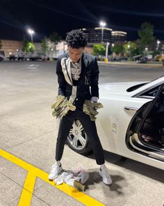 a man sitting on top of a pile of money next to a parked white car