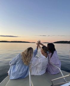 two women sitting on the back of a boat toasting with each other while looking out over water