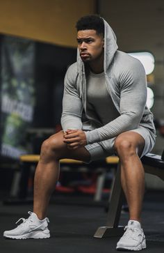 a man sitting on top of a bench wearing a gray hoodie and white sneakers