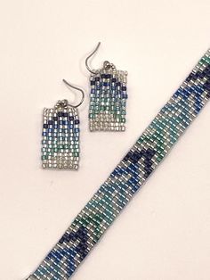 A chevron design in shades of blue on a silvery background. A woven beaded bracelet and earring set. The bracelet measures 7 inches, and 1/2 inch wide. The earrings hang approximately 1.5 inches. Adjustable Blue Jewelry With Silver Beads, Blue Metal Jewelry With Faceted Beads, Handmade Blue Metal Beaded Bracelets, Nickel-free Blue Metal Beaded Bracelets, Bracelet And Earring Set, Bead Earring, Chevron Design, Gloucester, Bracelet Set