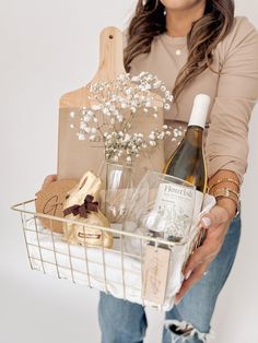 a woman holding a basket filled with wine, cookies and other items in front of her