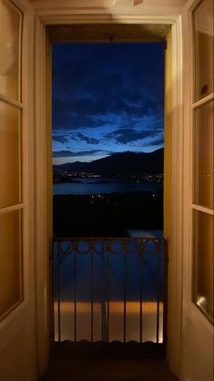 an open door leading to a balcony with a view of the water and mountains in the distance