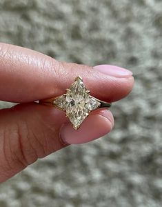 a woman's hand holding an engagement ring with a diamond in the shape of a square