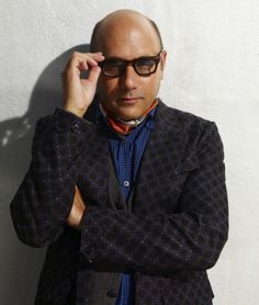 a bald man wearing sunglasses and a jacket leaning against a wall with his hands on his head