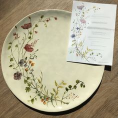 a white plate with flowers on it next to a piece of paper