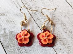 a pair of red and orange flower earrings on white wooden background with gold earwires