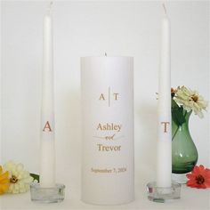 two white candles sitting on top of a table next to some vases and flowers