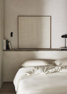 a bed with white sheets and pillows in a bedroom next to a wall mounted mirror