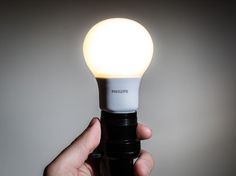 a person holding an illuminated light bulb in their left hand, on a gray background