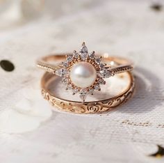 two wedding rings with pearls and diamonds on top of each other, sitting on a lace tablecloth