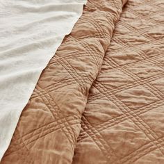 an unmade bed with brown and white quilting on it's side, next to a pillow