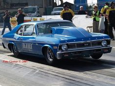 a blue car driving down a race track with people watching from the sidelines behind it