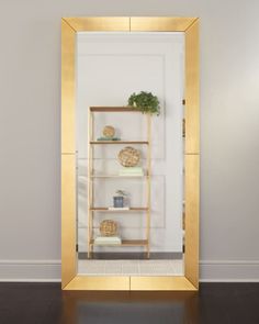 a gold framed mirror on the wall with shelves and plants in it, against a white wall