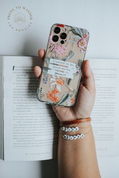 a person holding an iphone case with flowers on it and a book in the background