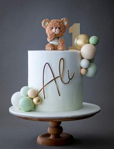 a teddy bear sitting on top of a white cake with gold and pastel decorations