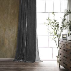 a room with a window, dresser and plant in the corner next to it on a wooden floor