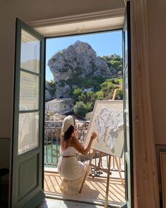 a woman in white dress painting on an easel