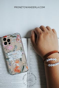 a person's hand resting on top of an open book next to a cell phone