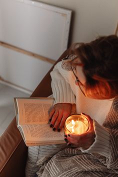 a woman reading a book and holding a lit candle