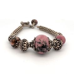 "Handmade Pink and Black Rhodonite Gemstones and Silver Beaded Bracelet  925 Solid Sterling Silver with a Toggle Clasp 8\" bracelet- Fits a larger wrist Beautiful and Unique Toggle Bracelet! Metal Content: 925 Sterling Silver Clasp: Toggle Clasp Measurements Length:  8\"  Width:  13/16\" (20mm) Weight: 51.52 Grams Marked: none Very Good pre-owned Condition Each piece is thoroughly examined and refinished as needed by our professional jewelers, tested to guarantee metal content,  graded by our in-house GIA (Gemological Institute of America) Graduate Gemologist, and inspected for quality before being carefully packaged and promptly shipped. Thank you for taking the time to shop with us! We have hundreds of more listings, with more being added every week! From necklaces to bracelets, the clas Handmade Beaded Bracelets In Sterling Silver With Fusion Style, Artisan Sterling Silver Bracelets With Round Beads, Fusion Style Jewelry With Silver Beads, Artisan Beaded Bracelets With Natural Stones In Sterling Silver, Artisan Sterling Silver Beaded Bracelet With Natural Stones, Artisan Silver Beaded Bracelets With Gemstones, Adjustable Sterling Silver Beaded Bracelets With Stones, Artisan Hand-strung Sterling Silver Beaded Bracelets, Artisan Sterling Silver Bracelet With Natural Stones