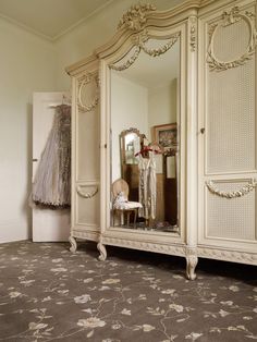 an ornate white armoire and mirror in a room with floral carpeting on the floor