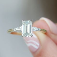 a close up of a person holding a ring with an emerald and baguette cut diamond