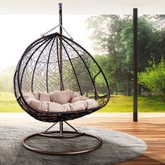 a hanging egg chair on a rug in front of a large window with an outside view