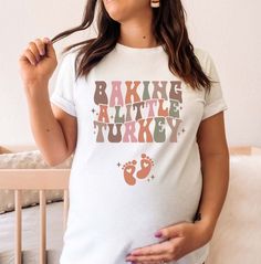 a pregnant woman standing in front of her crib wearing a t - shirt that says baking little turkey