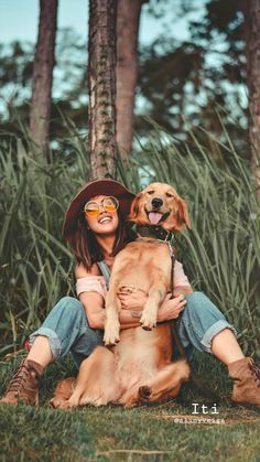 a woman sitting on the ground with her dog in front of some tall grass and trees