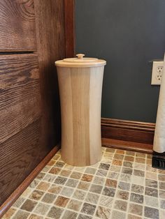 a wooden trash can sitting in the corner of a room next to a toilet paper dispenser