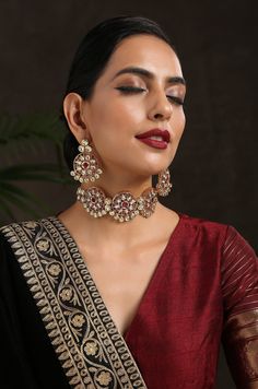 This exquisite design features a rich palette and beautiful kundan work. The top choker part is encrusted with red stones and dangling from it are several kundan units embellished with pearl trinkets. Necklace Closure - Adjustable Dori Earrings Closure - Push Back Style Tip - Being a strong supporter of the intersection of classic and contemporary, we love designs that are contemporary yet boast hints of traditional charm. This choker can be a great pair for traditional sarees, indo-wedstern dre Temple Jewelry With Zari Work For Party, Red Kundan Traditional Wear With Stone Work, Heavy Ruby Red Chandbalis, Saree With Choker Necklace, Heavy Red Ruby Chandbalis, Traditional Ruby Meenakari Kundan Necklace, Traditional Ruby Kundan Necklace With Meenakari, Celebration Ruby Kundan Necklace With Chandbali Shape, Diwali Party Jewelry With Zari Work