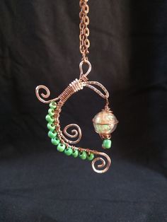 "Copper color wire wrap design featuring green seed beads and a swirling green glass bead \"lantern\" Indulge your whimsical side with this charming and uniquely one of a kind accessory, perfect for adding a bit of playful magic to any outfit! All my pieces are handmade creations. The item pictured is the item that will be shipped to you, though colors may vary slightly from picture due to differences in monitor settings.  Check out my shop for more charms and creative jewelry, or message me if you have a specific idea in mind!" Green Copper Spiritual Necklace, Spiritual Green Copper Necklace, Green Copper Hand Wrapped Necklaces, Green Hand Wrapped Copper Necklace, Whimsical Green Pendant Jewelry, Green Bohemian Copper Wire Necklace, Whimsical Wire Wrapped Jewelry For Crafting, Handmade Green Artsy Necklace, Whimsical Green Nickel-free Jewelry