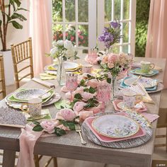 the table is set with pink flowers and plates