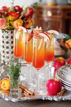 three glasses filled with drinks sitting on top of a silver tray next to apples and cinnamons