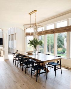 a dining room table with six chairs and a vase on the table in front of large windows