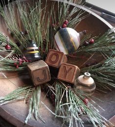 a wooden block with the word joy on it sitting next to some ornaments and pine needles