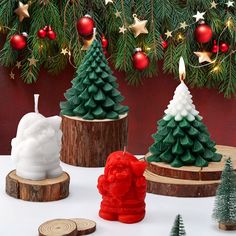 three small christmas trees sitting on top of wooden stumps next to candles and ornaments