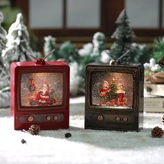 two small tvs sitting on top of a snow covered ground next to pine cones