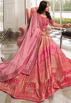 a woman sitting in a chair wearing a pink and gold lehenga