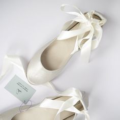 two pairs of white shoes with ribbons tied around the toes and heel, on a white surface