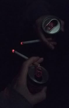 a person holding two cans in their hands at night with red light coming from them